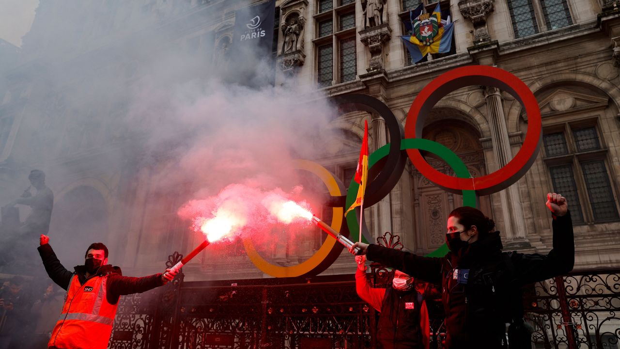 Protestors light red flares in front of the Olympic rings in Paris.